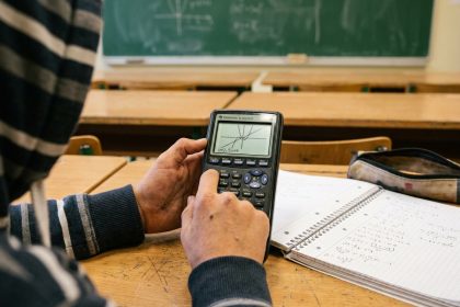 Élève de collège utilisant une calculatrice scientifique graphique sur un bureau en bois entouré de cahiers de mathématiques