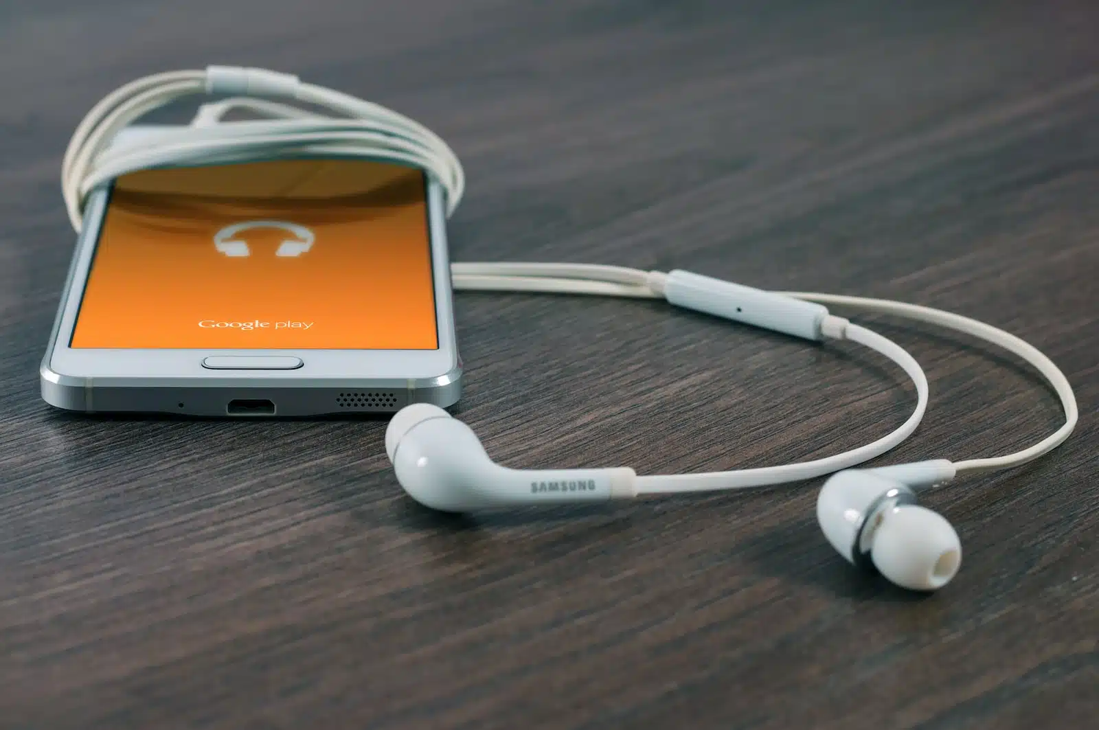 white Samsung Android smartphone turned beside white earbuds on brown board